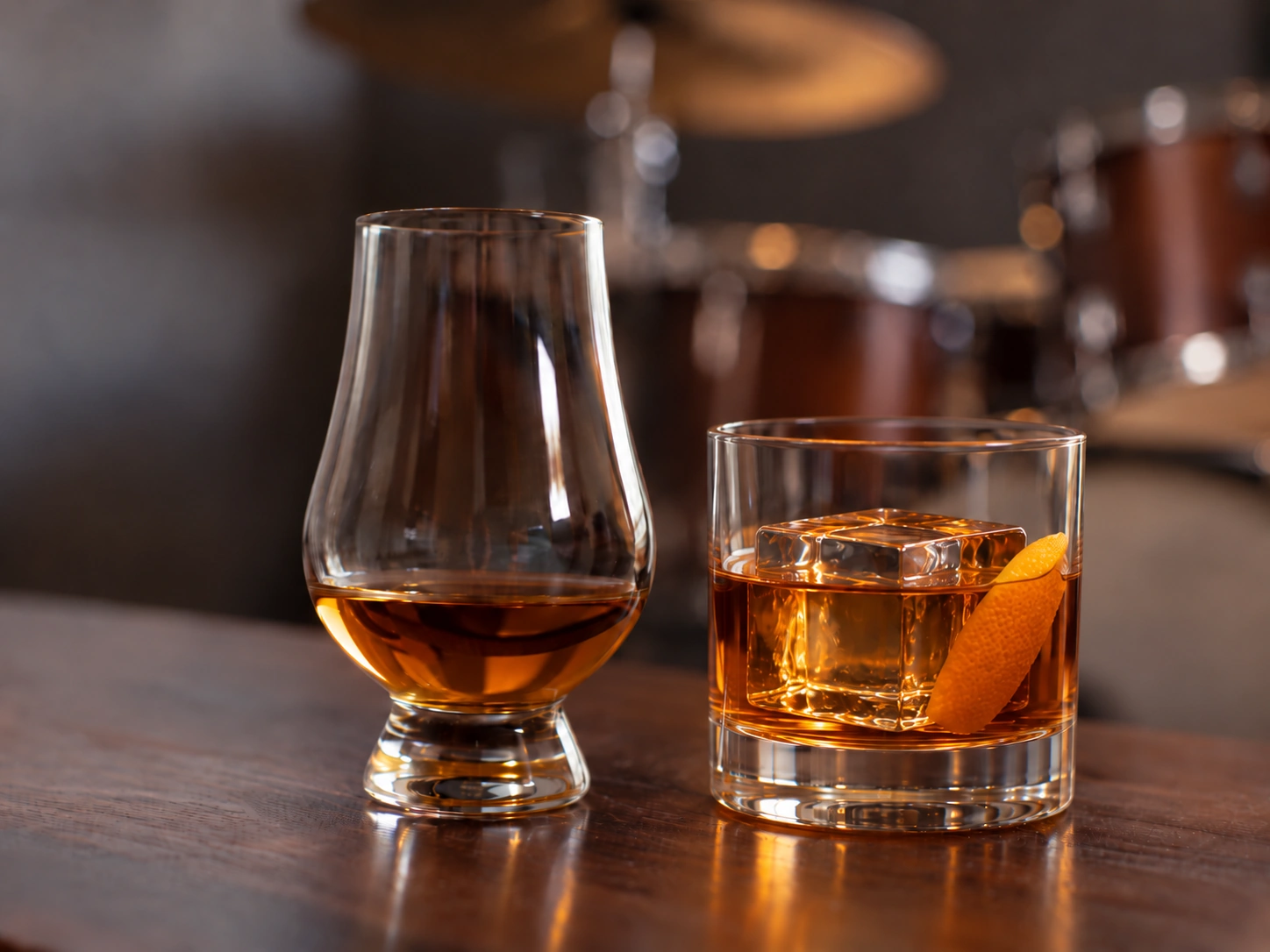 A neat pour and whiskey cocktail with crystal-clear ice, with a drum kit softly blurred in the background